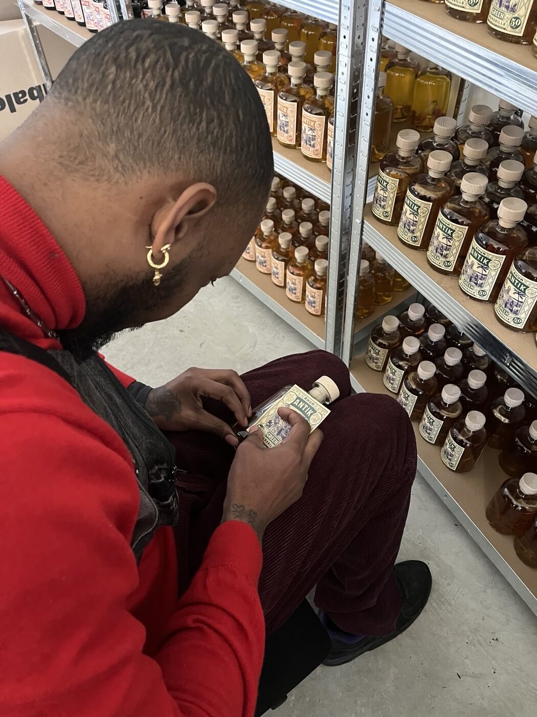 Marvin étiquette une bouteille ANTIK à la main devant les casiers de l'atelier